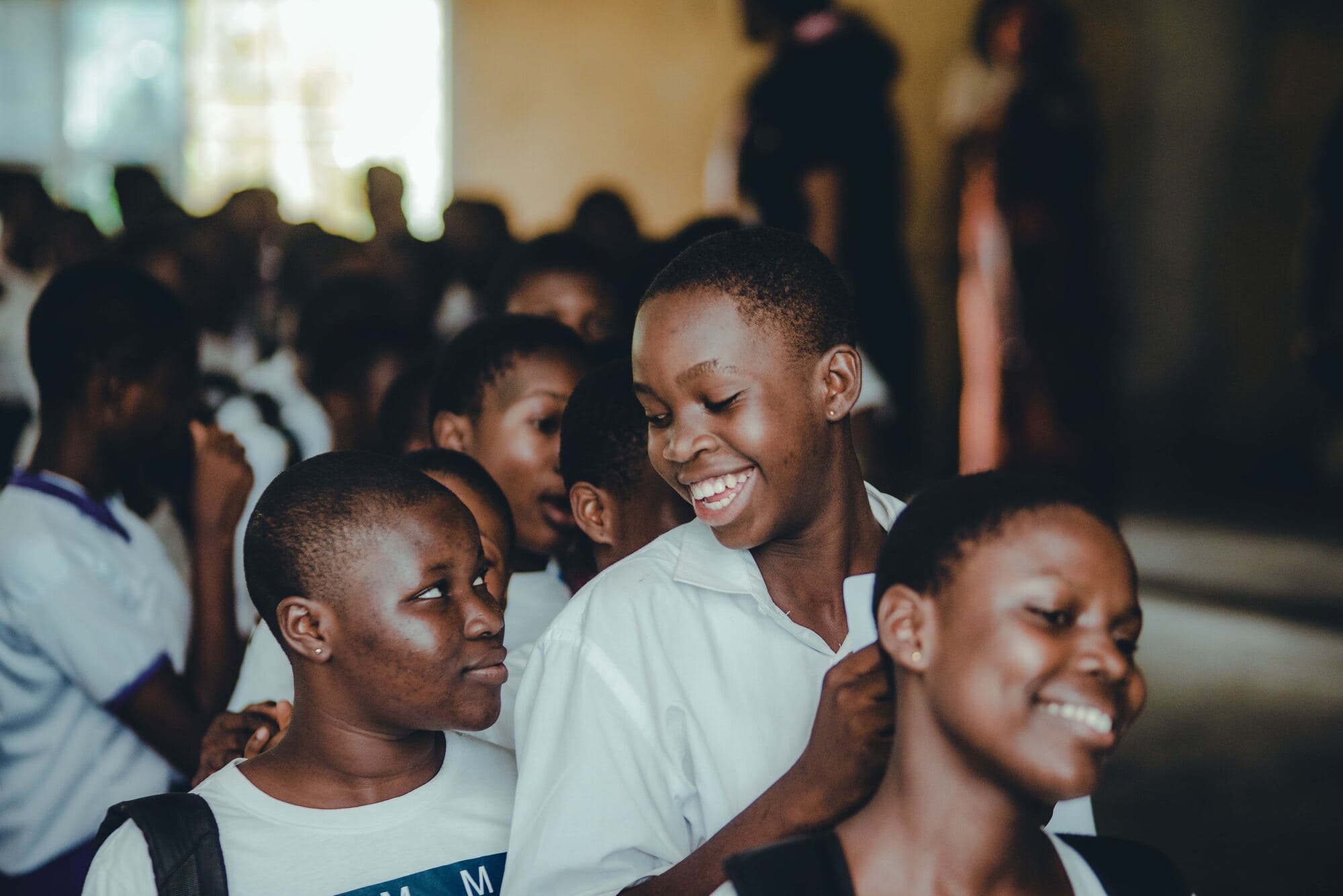 Teenage girls in white school shirts laugh together in a crowded school hall