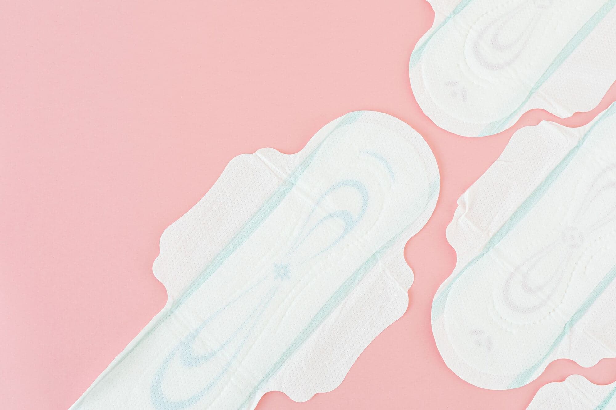 White sanitary pads with wings laid out on a soft pink background
